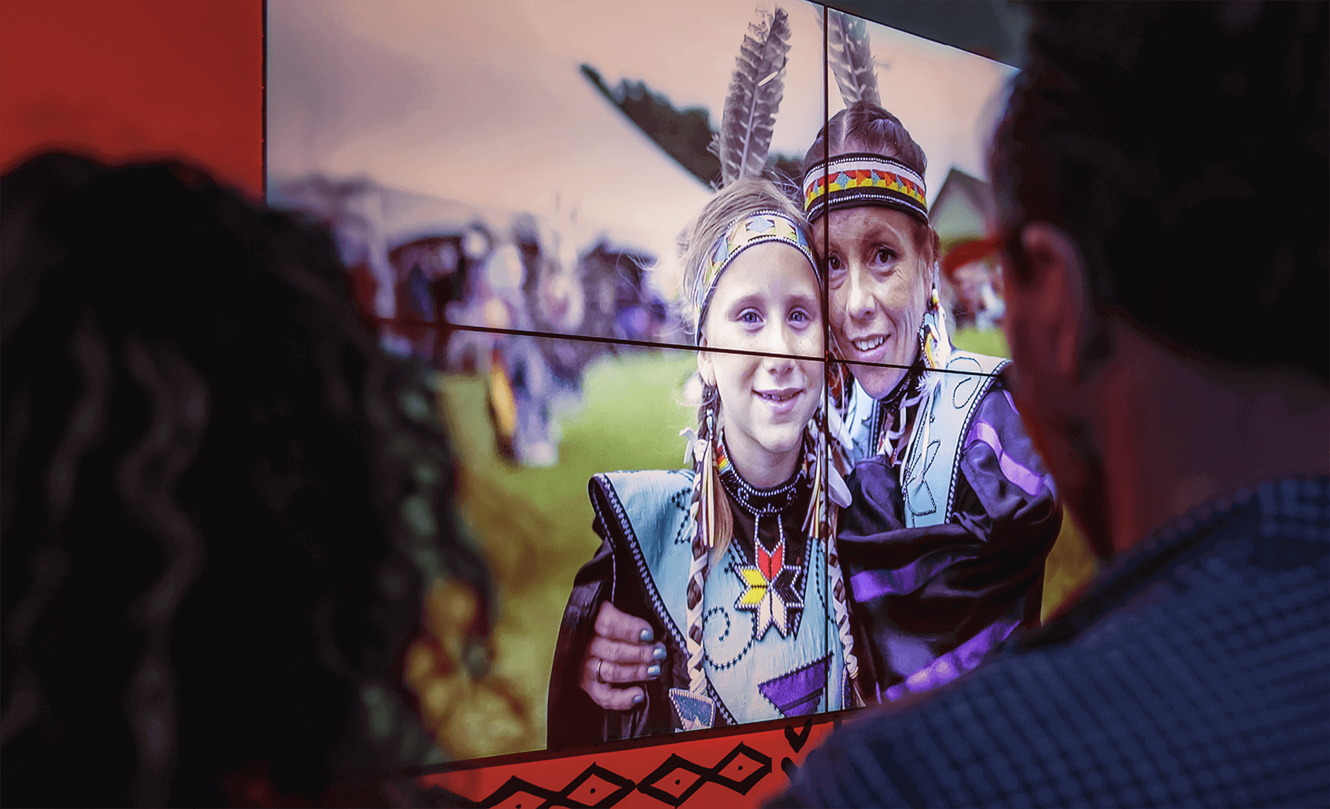 Identité visuelle | Participants en habits traditionnels autochtones sur un écran géant | TAQ